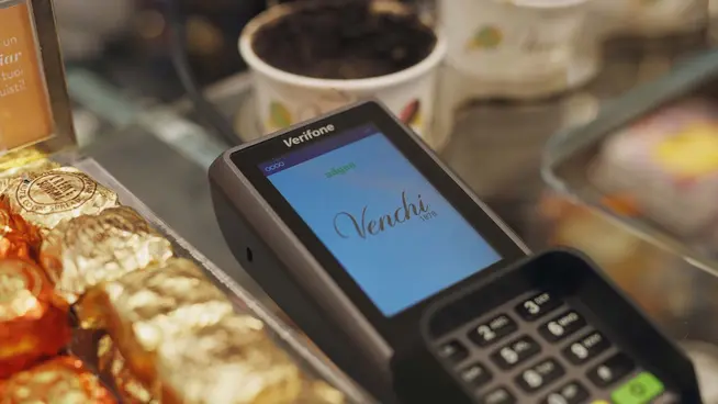 Vue rapprochée d'un terminal de paiement par carte avec un écran coloré sur un comptoir de magasin.