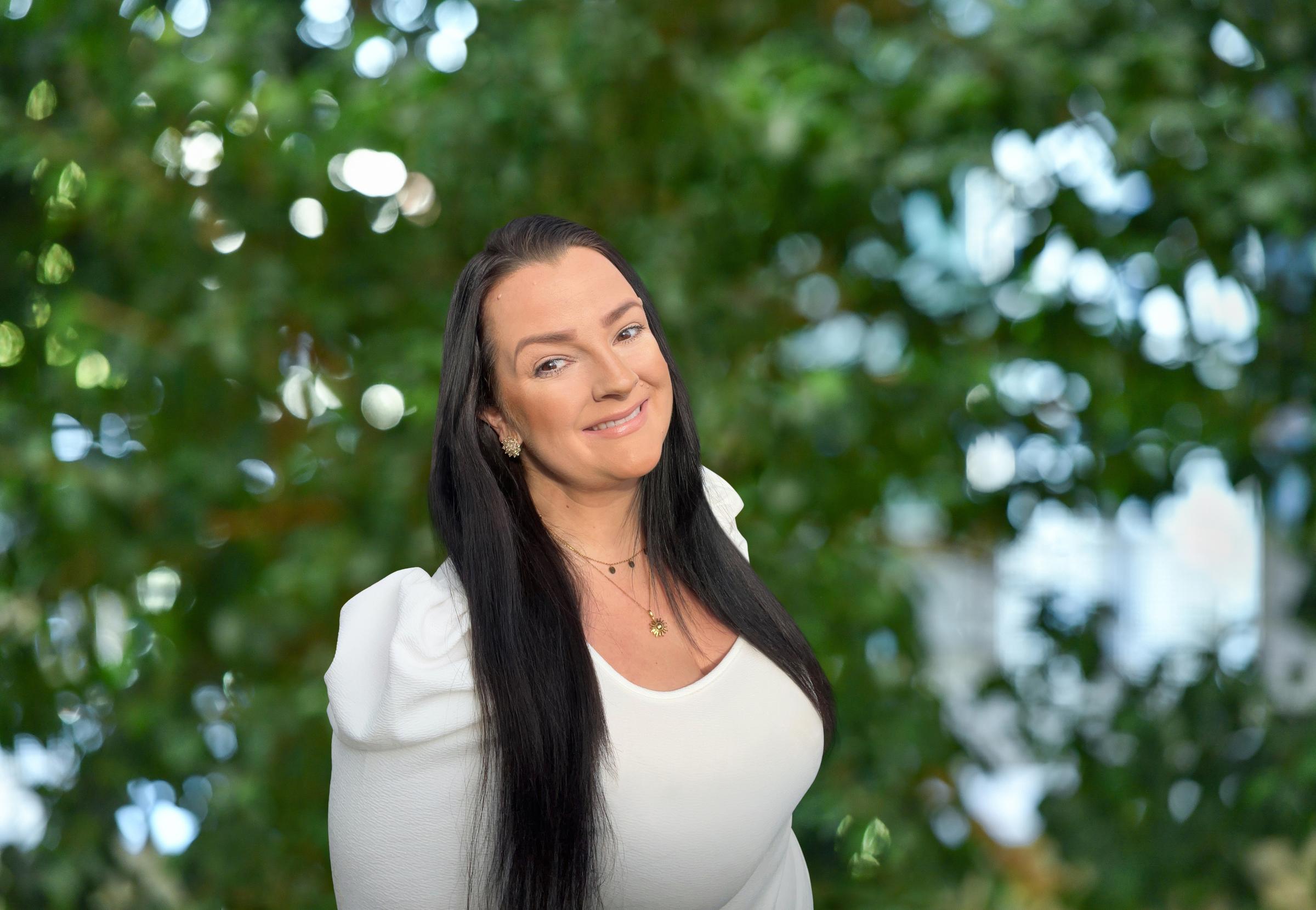 Frau mit dunklem Haar in weißer Kleidung vor grüner Naturkulisse, Premium Cluburlaub bei Aldiana