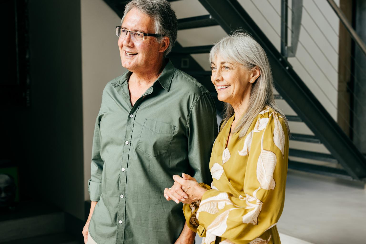 Zwei Menschen stehen in einem modernen Innenraum, halten Hände und unterhalten sich.
