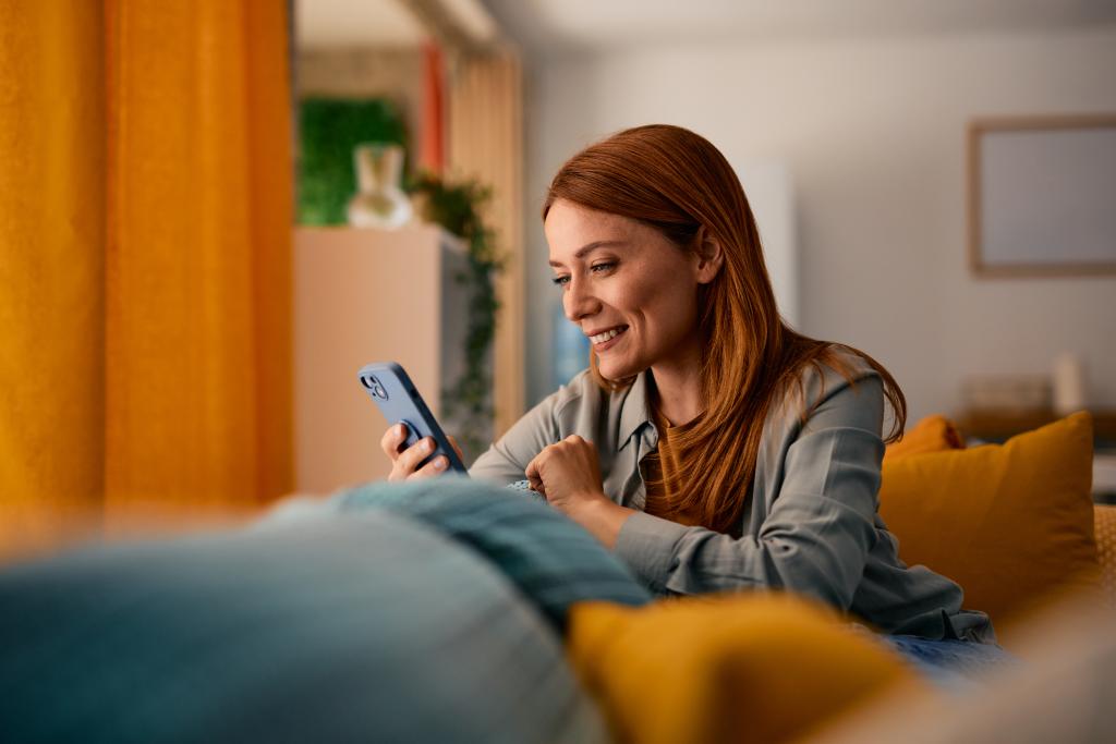 Frau nutzt Smartphone im Wohnzimmer, angenehme Atmosphäre, moderne Einrichtung.