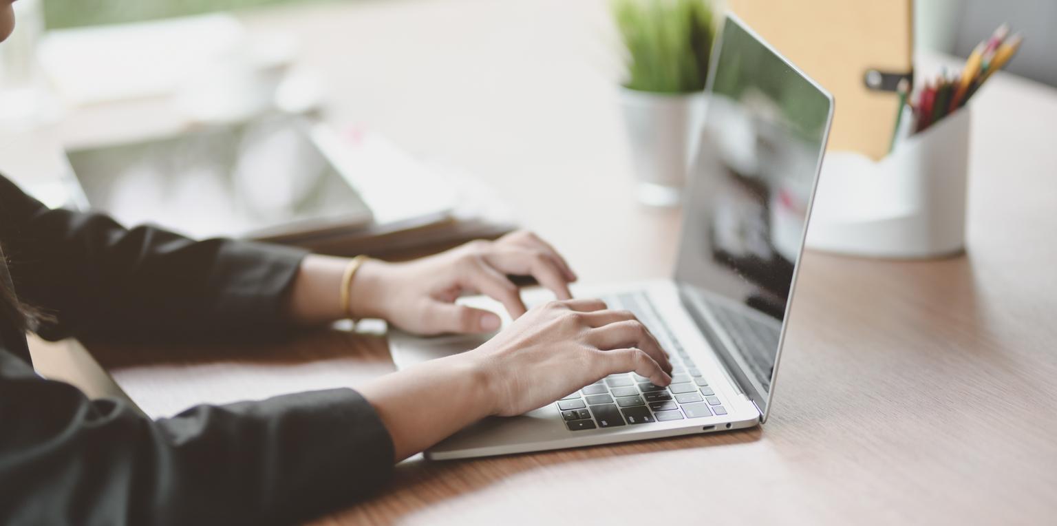 Cropped view of businesswoman typing on keyboard laptop in modern workplace