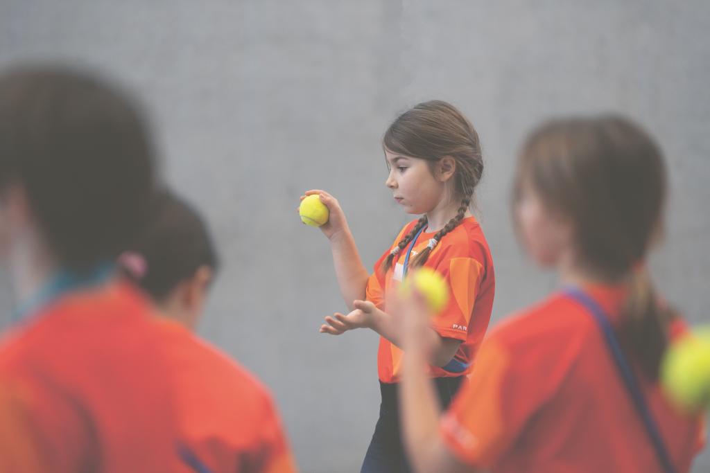Kinder beim Tennis, lachend und in roten Sportshirts, auf einem Court.