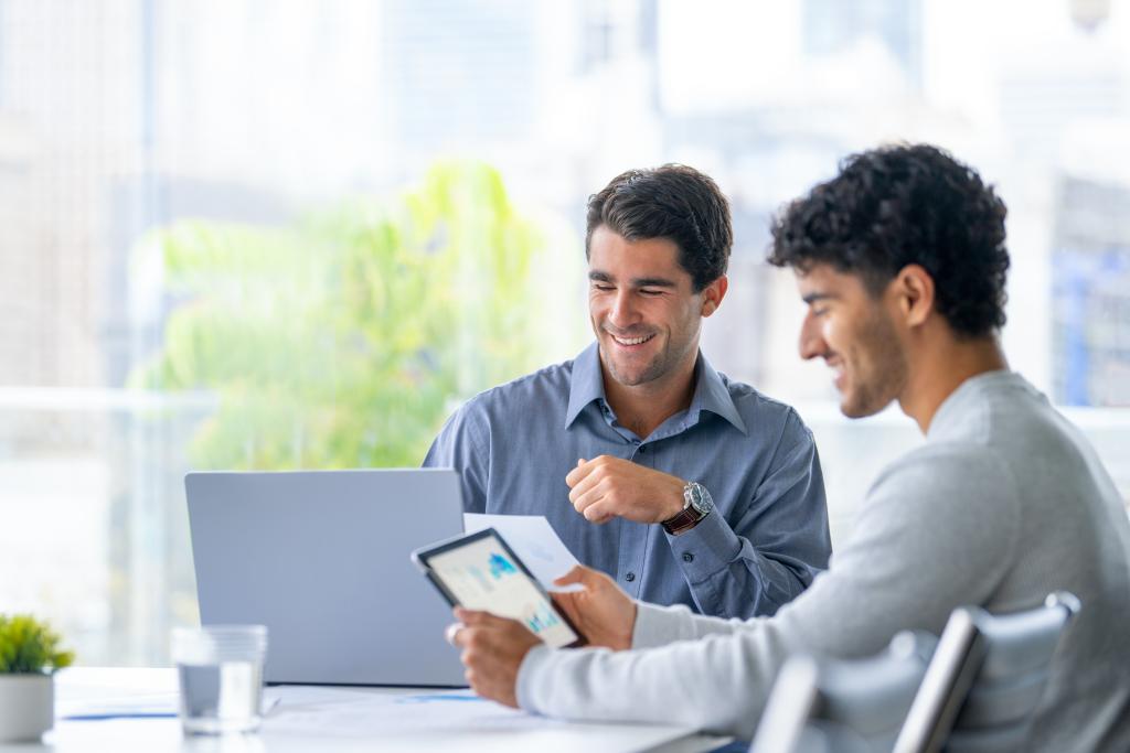 Zwei Geschäftsleute bei einem Meeting mit Laptop und Smartphone in einem Büro.