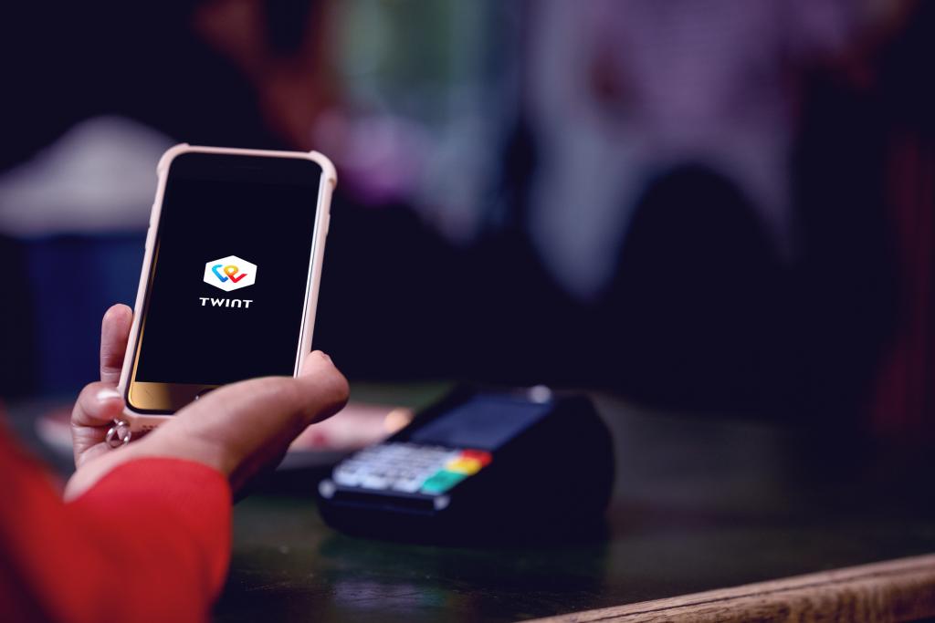 Person hält Smartphone mit TWINT App beim Kartenlesegerät der BLKB an der Theke