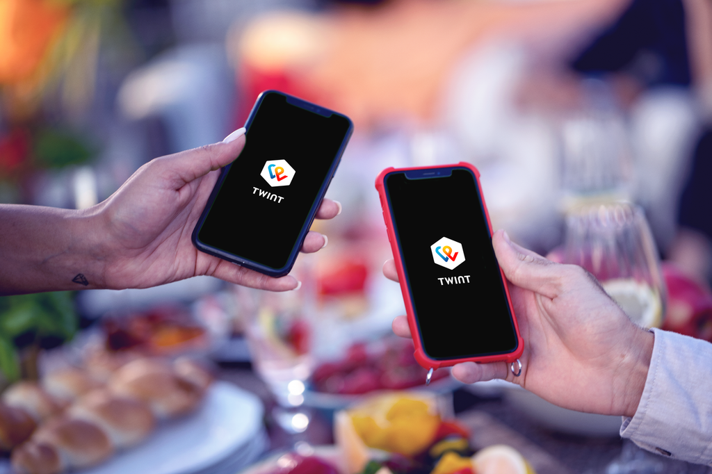 Hände halten Handy mit der Twint App beim geselligen Essen und Trinken.
