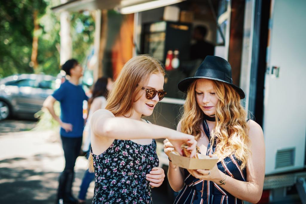 Junge Frauen genießen Essen an einem Foodtruck in entspannter Atmosphäre.