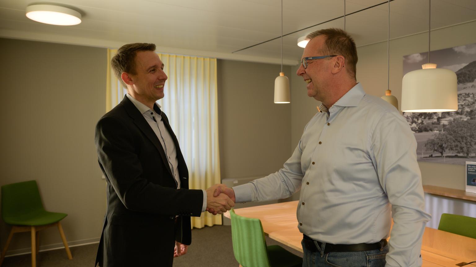 Zwei Männer schütteln sich höflich die Hand in einem modernen Büro.