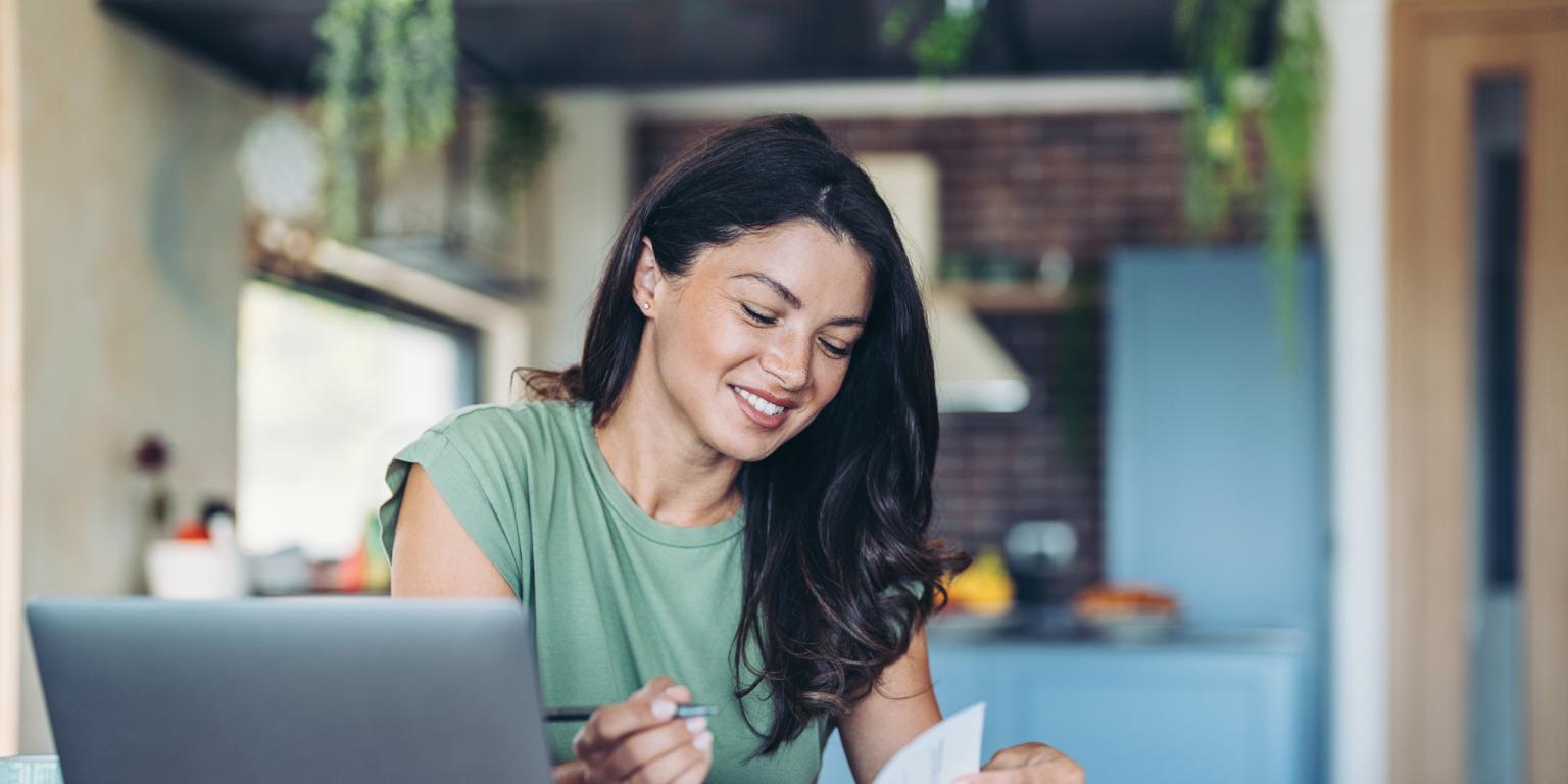 Frau arbeitet an Dokumenten mit einem Laptop, lächelnd in einem gemütlichen Homeoffice-Setting.