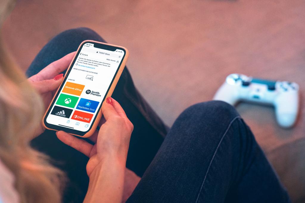 Person nutzt Smartphone mit BLKB Online Banking App, beim Spielen mit Controller im Hintergrund