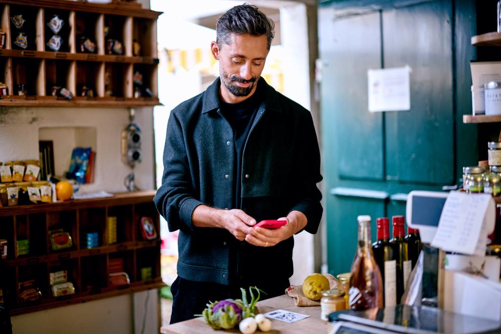 Mann mit Smartphone hinter der Kasse in einer Ladenumgebung der BLKB.