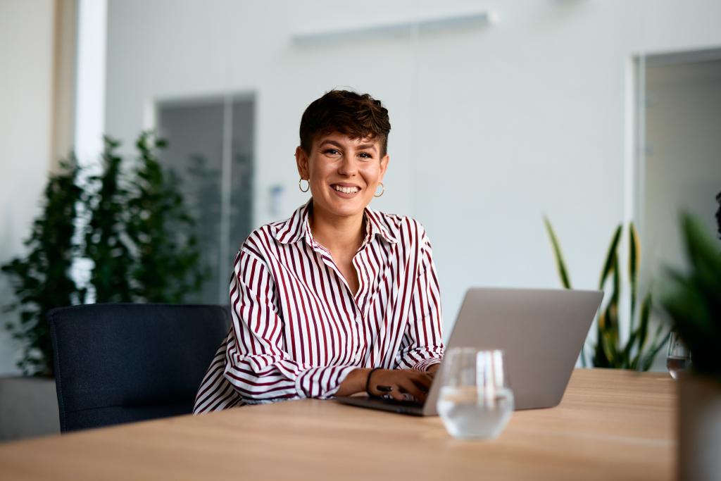Frau arbeitet an Laptop im modernen Büro, hinter ihr Pflanzen und helle Wände