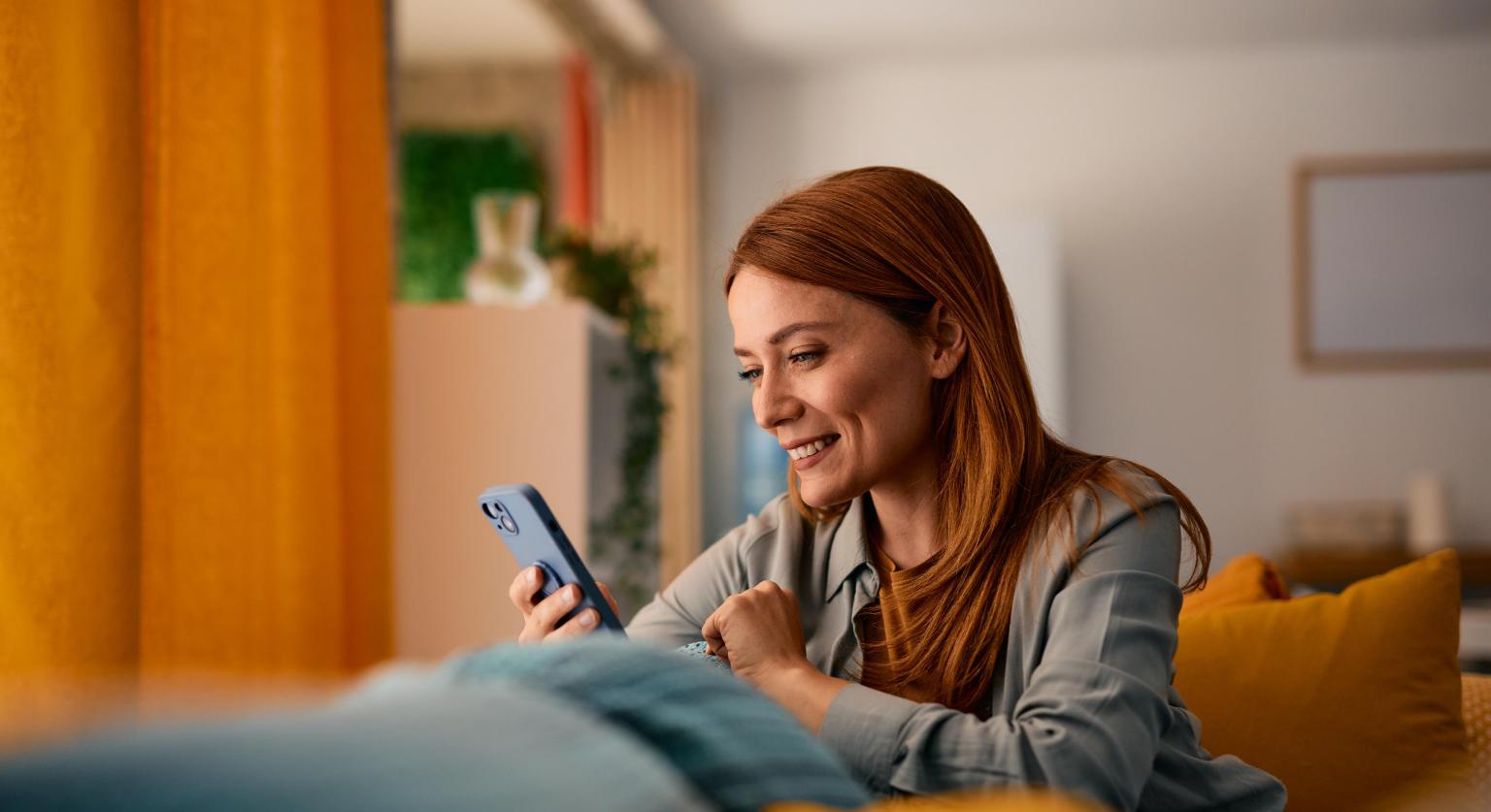 Frau nutzt Handy im Wohnzimmer bei gemütlicher Atmosphäre und moderner Einrichtung.
