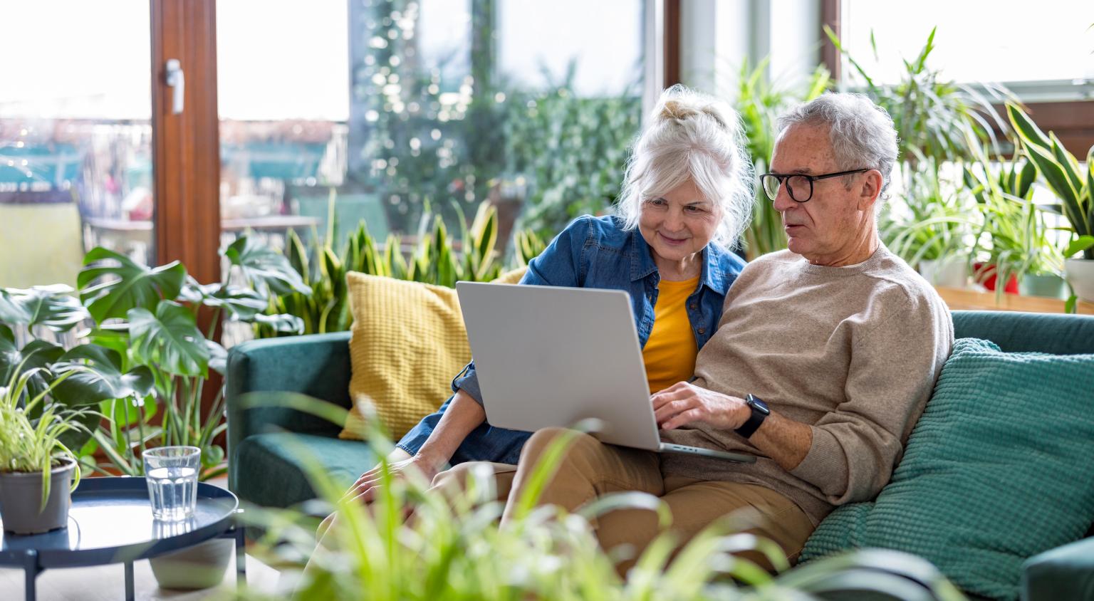 Senior couple using laptop while sitting on sofa in living room at home aus dem Artikel Abschaffung des Eigenmietwerts in der Schweiz