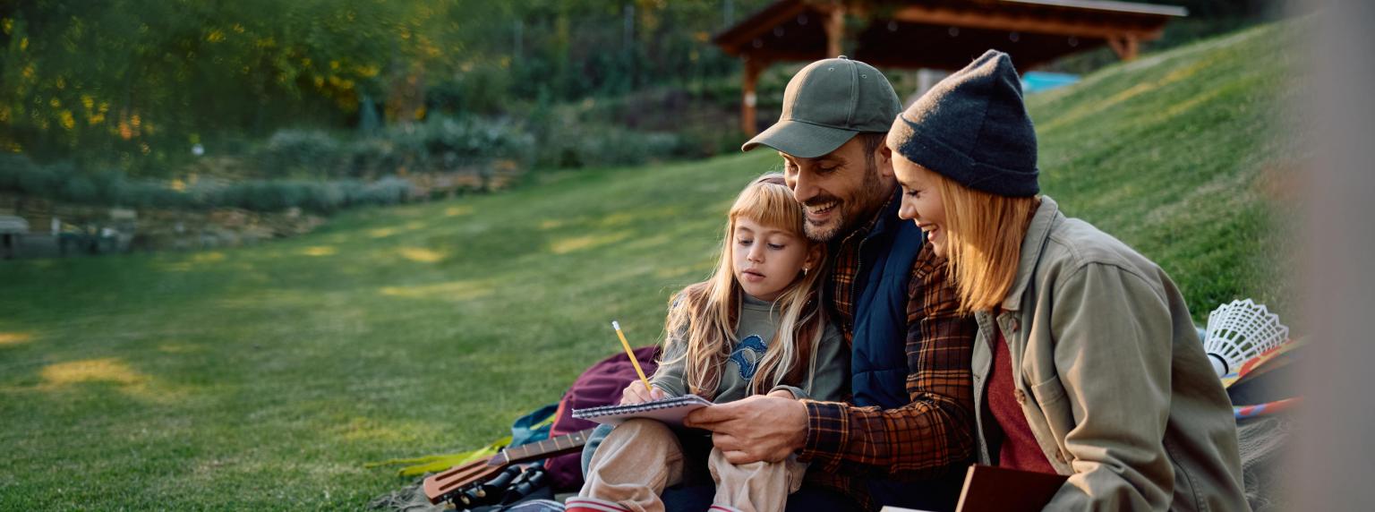 Drei Menschen sitzen gemütlich im Grünen beim Lesen und Sprechen.