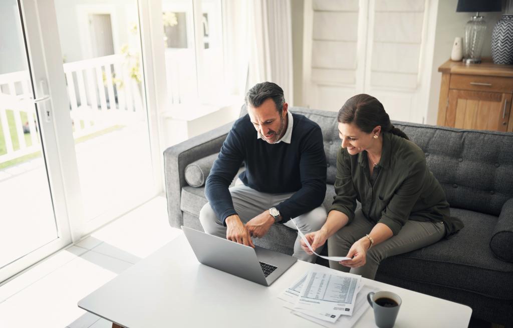 Zwei Personen arbeiten am Laptop mit Dokumenten in einem hellen Wohnzimmer