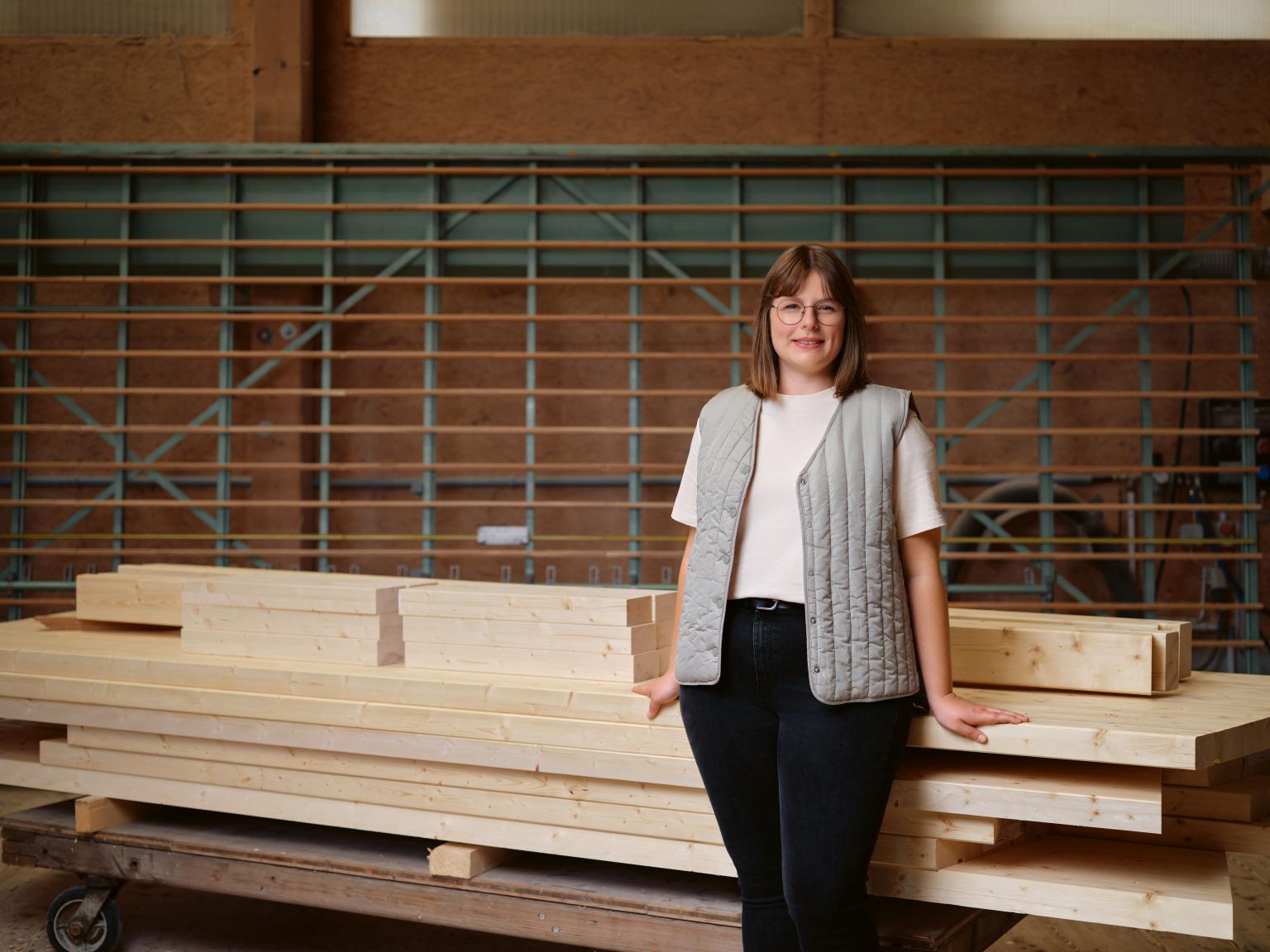 Frau im Bauunternehmen vor Holzmaterialien und Baugerüst in einer Holzhalle