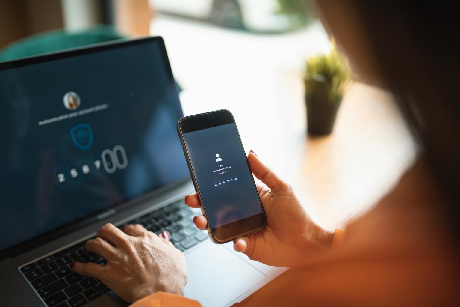 Person, die sich auf dem Laptop anmeldet, während sie das Smartphone zur Authentifizierung verwendet. aus dem Artikel Gemeinsam für mehr Sicherheit im Zahlungsverkehr