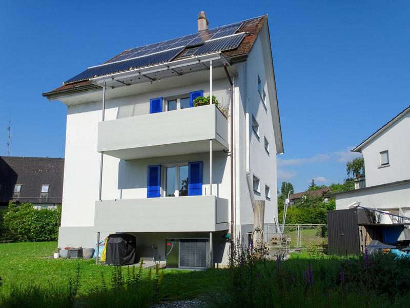 Einfamilienhaus mit Balkon und Solarpanels unter klarem Himmel.