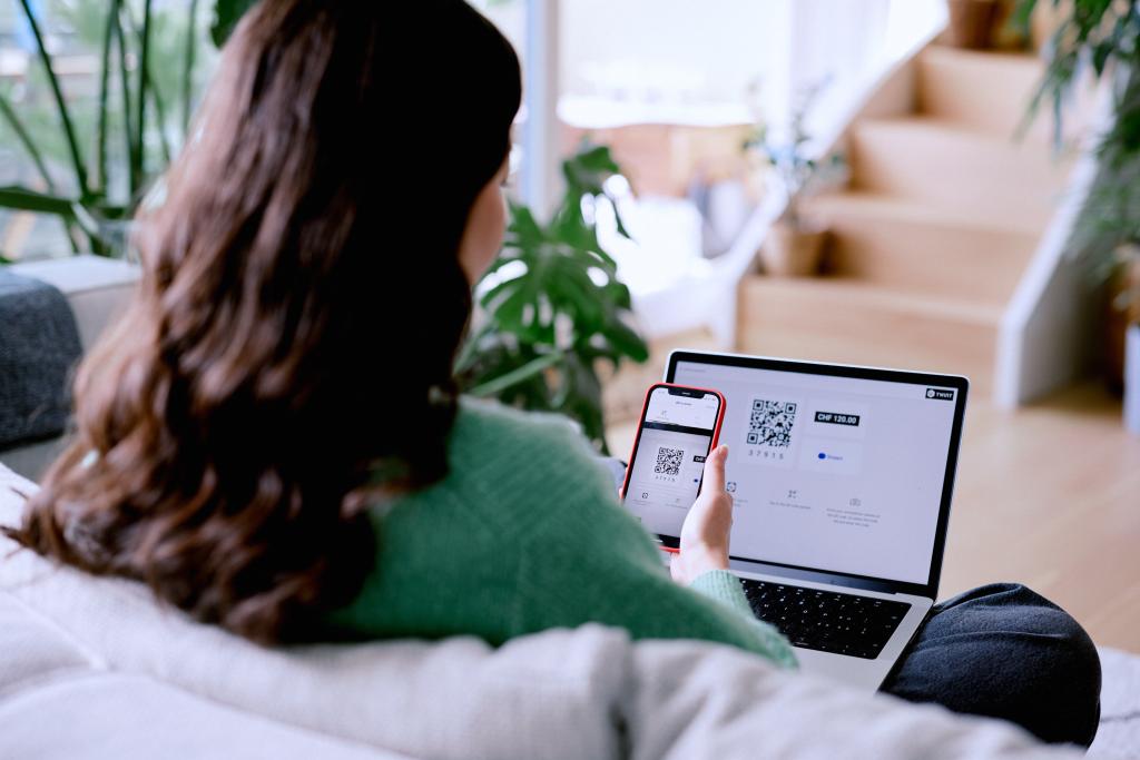 Eine Person scannt QR-Codes auf einem Laptop und Smartphone für die BLKB.