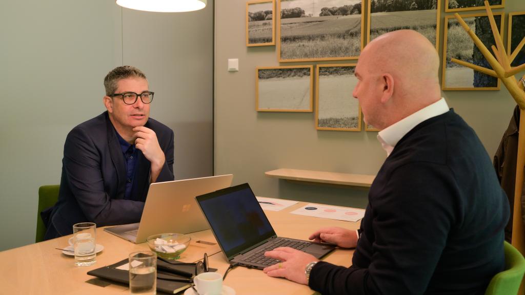 Zwei Männer sprechen in einem modernen Besprechungsraum mit Laptops.