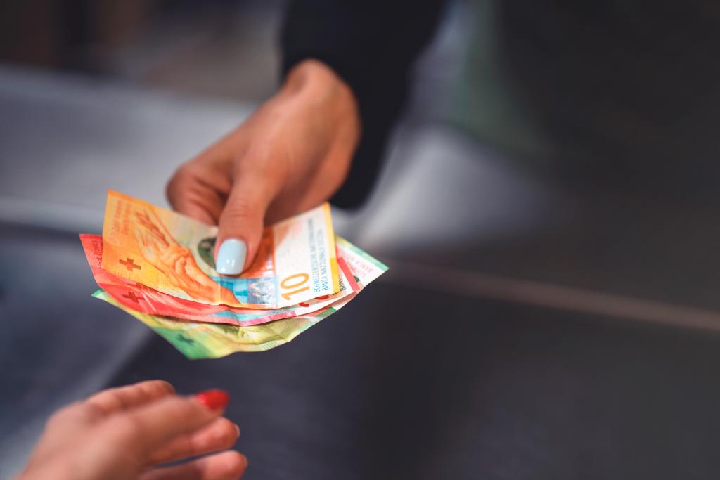 Eine Person übergibt Geldscheine an eine andere Hand bei BLKB in Basel.