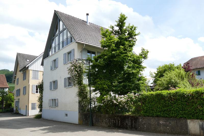 Ein traditionelles Gebäude mit einem geneigten Dach und üppigem Grün, das es umgibt.