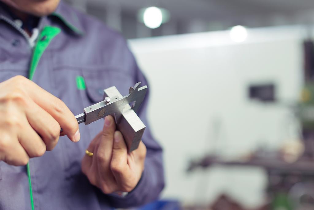 Man misst mit einer Messschraube Metallteile in einem Werkstattumfeld.