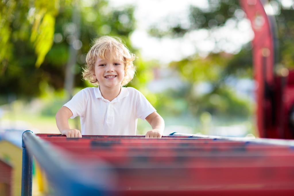 Kind mit weissem T-Shirt auf bunten Klettergerüsten. 