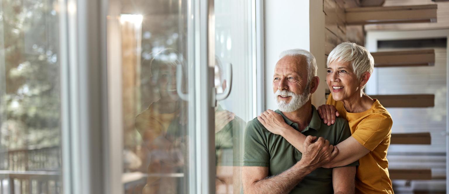 Zwei Personen umarmen sich freundlich hinter einem großen Fenster.