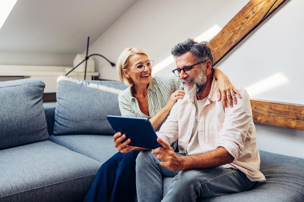 Zwei Personen sitzen entspannt auf einer Couch und schauen gemeinsam ein Tablet an