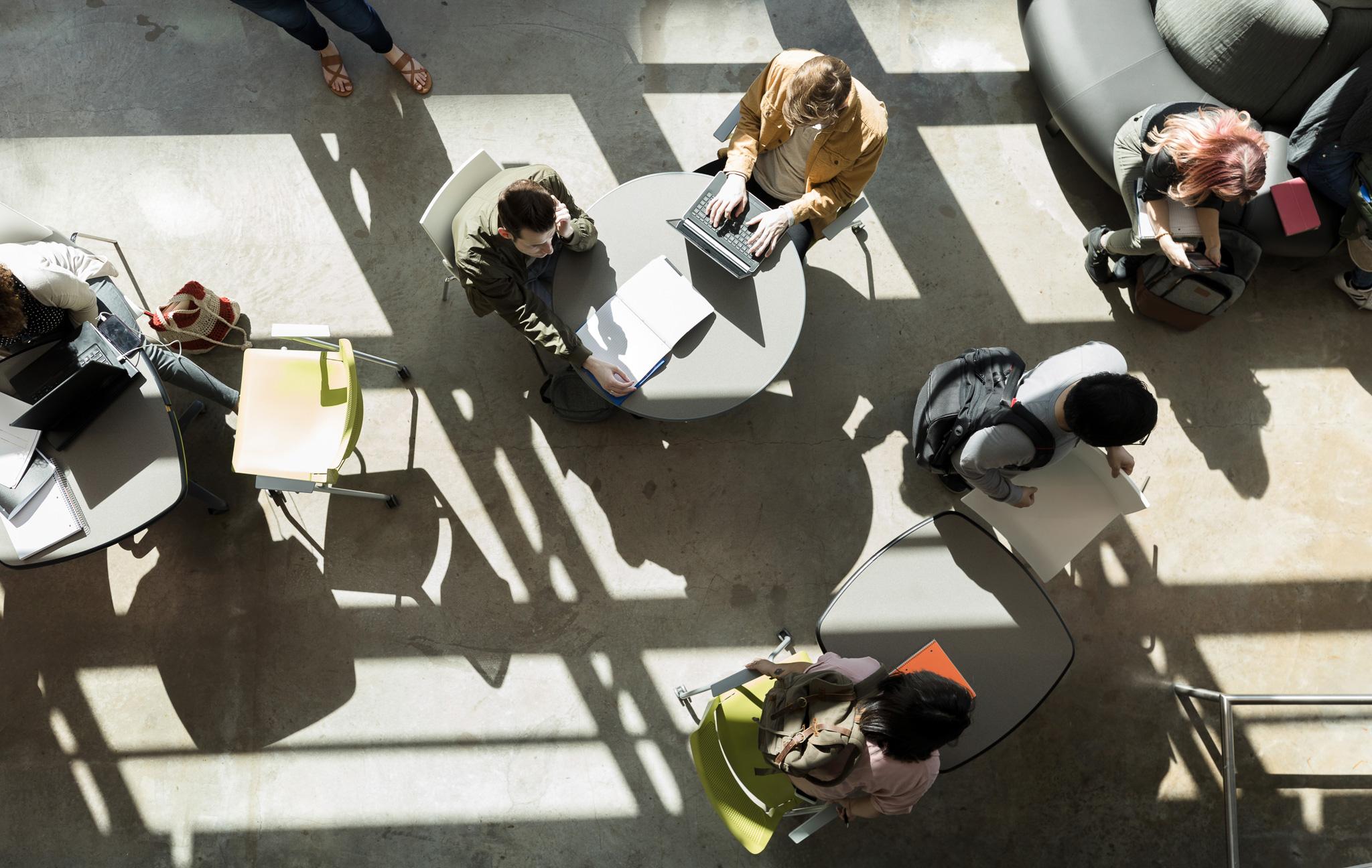 Eine Draufsicht auf eine multiethnische Gruppe von College-Studenten, die in der Lobby des Unterrichtsgebäudes an verschiedenen Projekten und Hausaufgaben arbeiten.