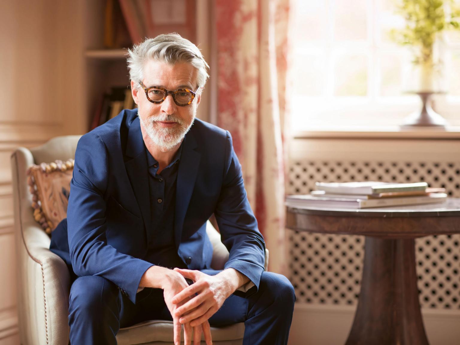 Businessman sitzt in einem eleganten Raum mit Büchern und einem runden Tisch.