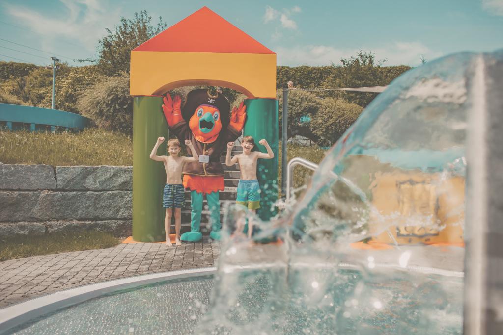Zwei Kinder mit Clown-Charakter an Wasserspiel, im Freien, sonniger Tag, spielend.