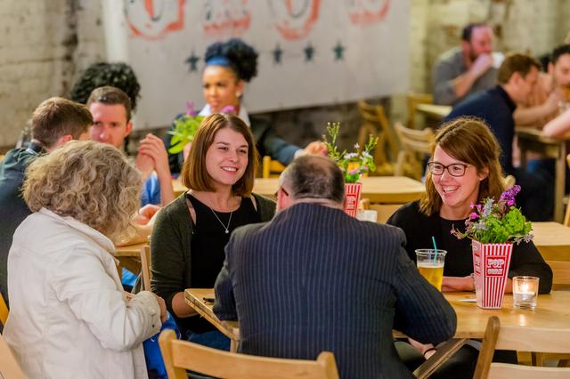 A group of people sat on wooden seating enjoying food and drinks