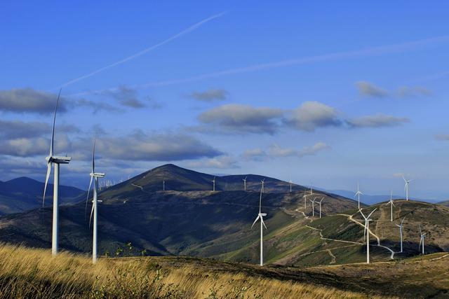 Blue skies with windmills that are generating electricity on green hills.