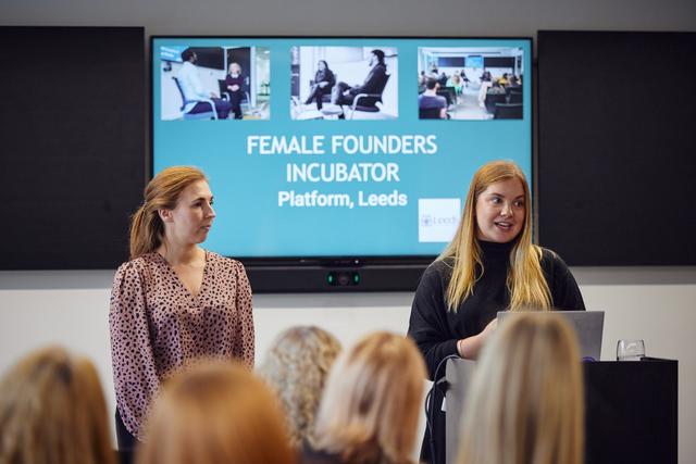 two women stood in front of tv screen with female founders incubator written on it