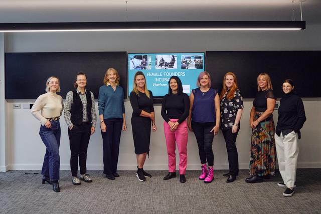group of female founders standing at front of room in front of a tv screen