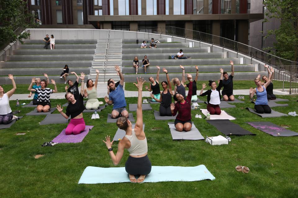 A group of people taking part in a yoga class on Symphony Park at Circle Square, they are reaching towards the sky with one hand on yoga matts