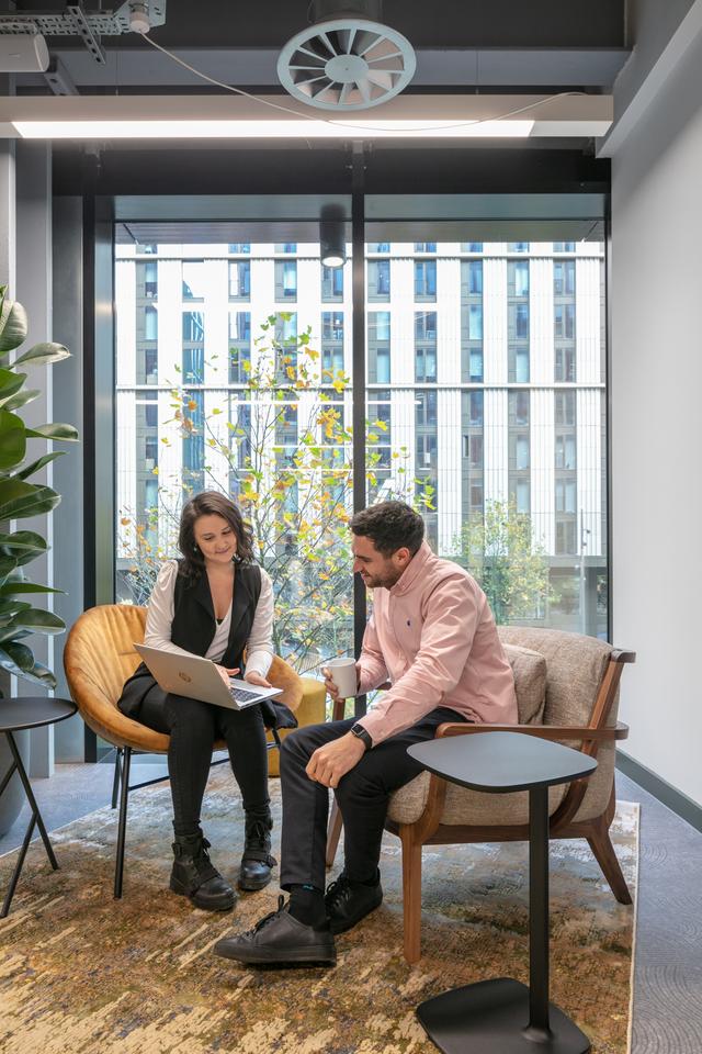 Two people sat down in a lounge area looking at one laptop together