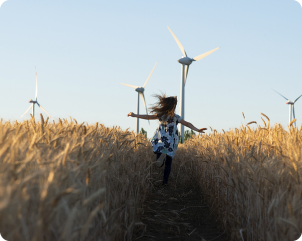 A girl running amongst the hay with wind turbines in the back ground