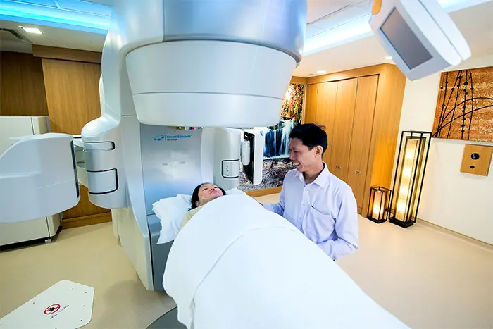 A doctor smiling reassuringly at a patient lying on a radiation machine getting ready for treatment