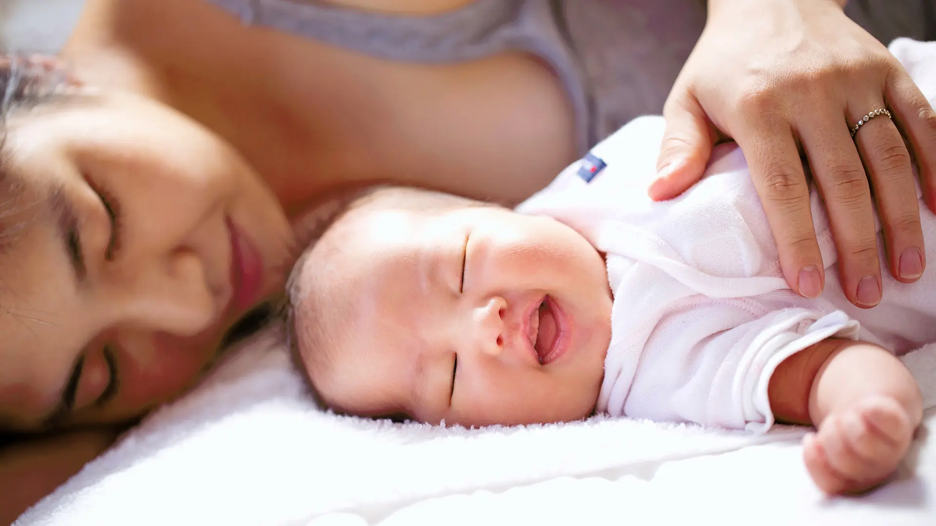 Mother lies down with her newborn and with her hand on its torso