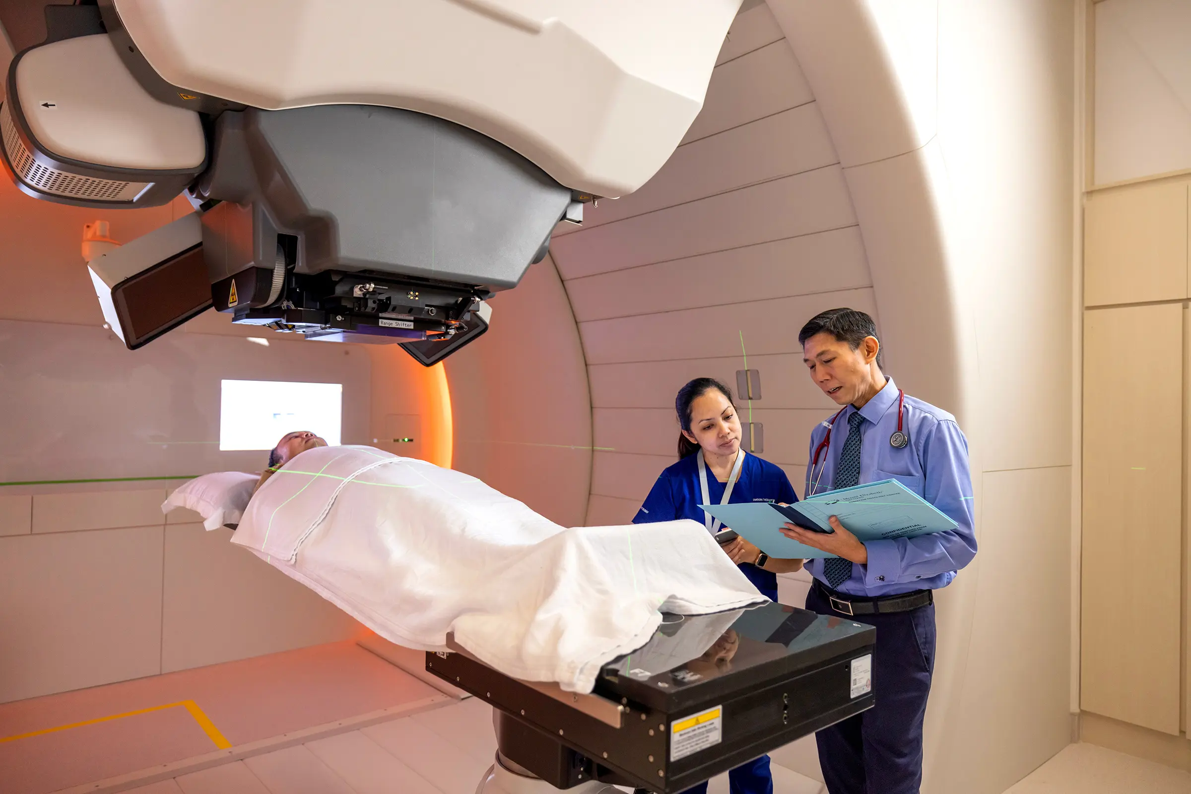 A doctor and his nurse reassuring a patient who is lying on the proton therapy machine