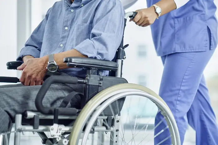 A patient in a wheelchair being assisted by a nurse in medical scrubs
