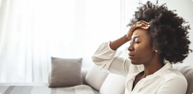 Woman sitting on a couch holding her forehead in distress, representing the gut-brain connection and how gut microbiome diversity may influence emotional well-being and depression.