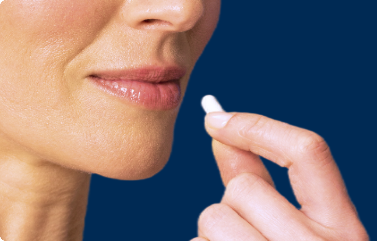 Close-up of a woman's face and hand as she holds a white capsule near her lips, ready to take a supplement, with a clean blue background.