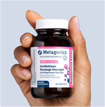 A hand holds a bottle of HerWellness™ Recharge Overnight, a women’s sleep and stress formula. The label is clearly visible, emphasizing natural ingredients like magnesium for relaxation, holy basil, and adaptogens for sleep. This supplement supports hormone balance for women, cortisol balance, nervous system support, muscle relaxation, and stress recovery—making it a smart, natural solution for restful nights and resilient days.