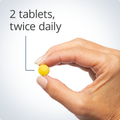 Hand holding a small yellow tablet, indicating a recommended dosage of two tablets twice daily.