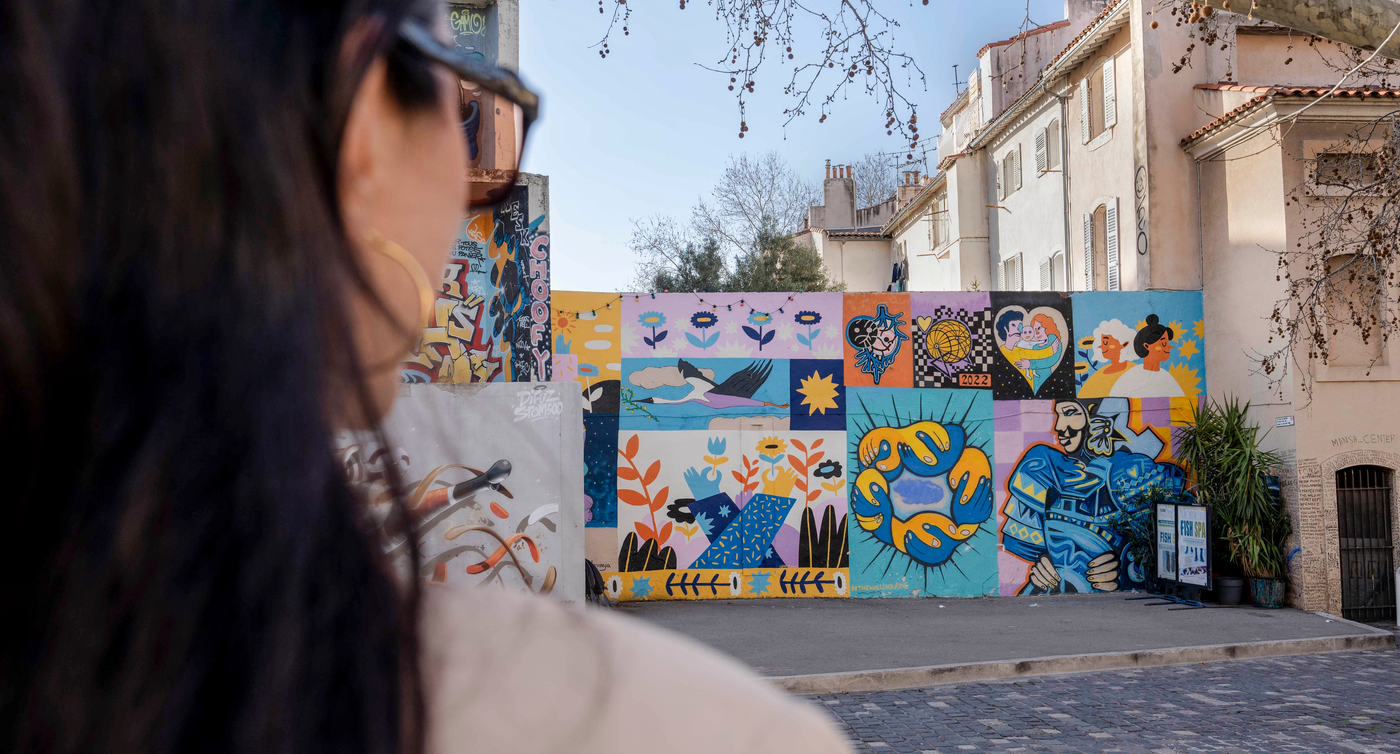 Eine Person betrachtet ein lebendiges Wandgemälde im Le Panier Viertel, ein Zeugnis der lebhaften Kunstszene und der Wertschätzung für urbane Kreativität in Marseille.
