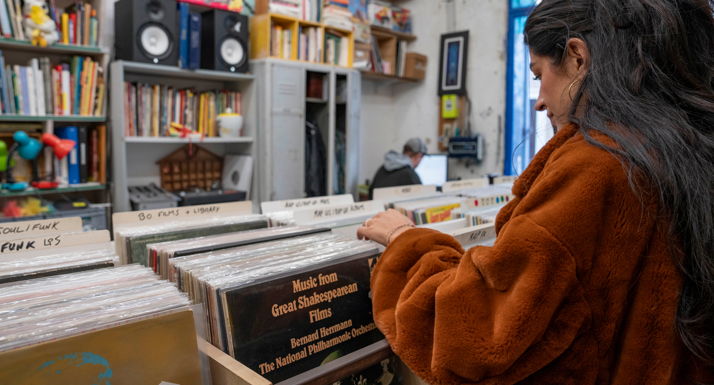 Eine Person durchsucht sorgfältig die Sammlung verschiedener Vinylplatten in einem kleinen, mit Büchern und Musik gefüllten Laden.